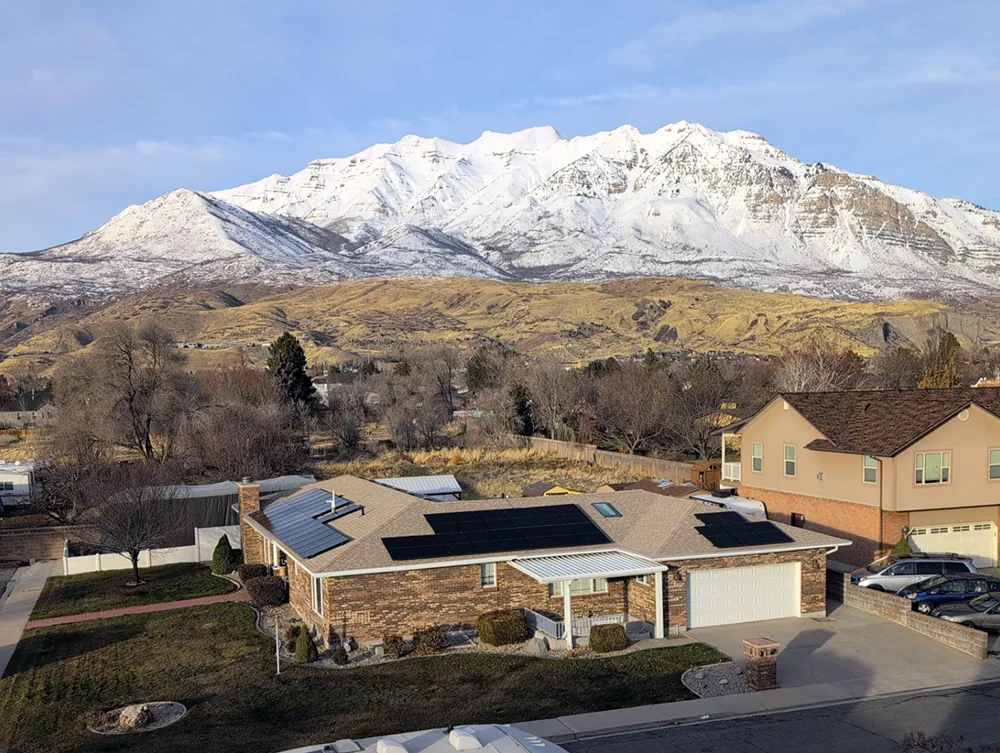 drone image of a house with solar panels and a snow covered mountain in the background